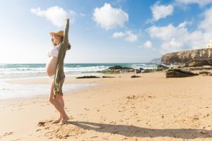 Femme enceinte vêtue d’un maillot de bain de grossesse sur une plage de sable et de rochers